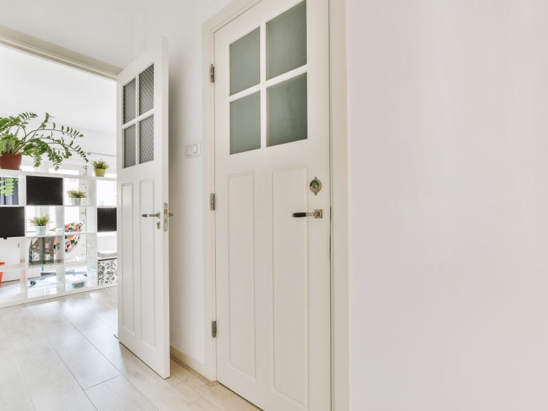 Light narrow hallway with doors in white walls and glowing lamp over lumber floor